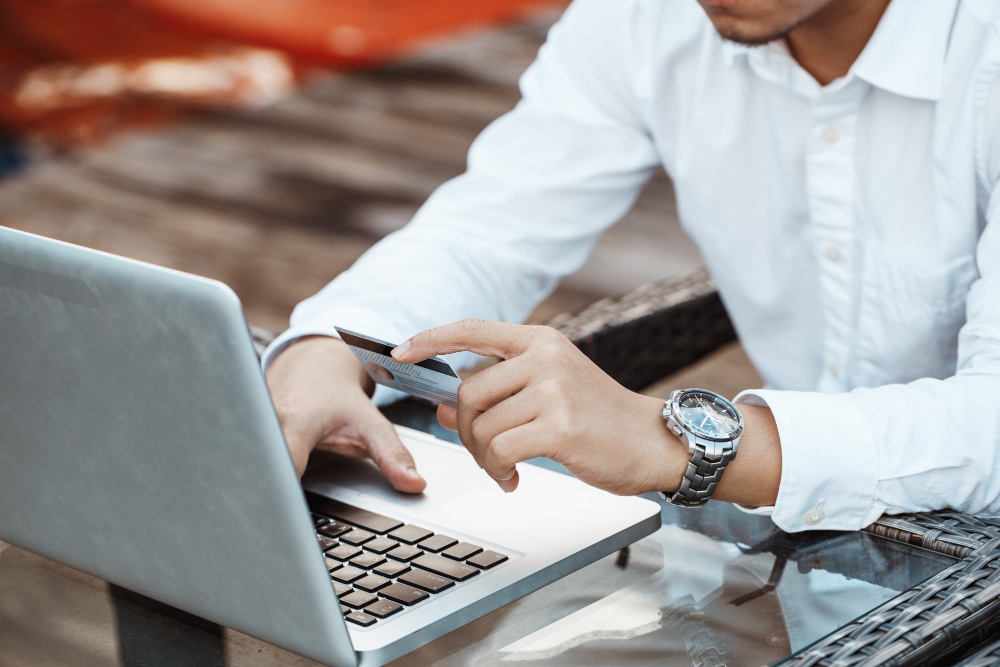 Mann am Laptop sitzend mit einer Bankkarte in der Hand